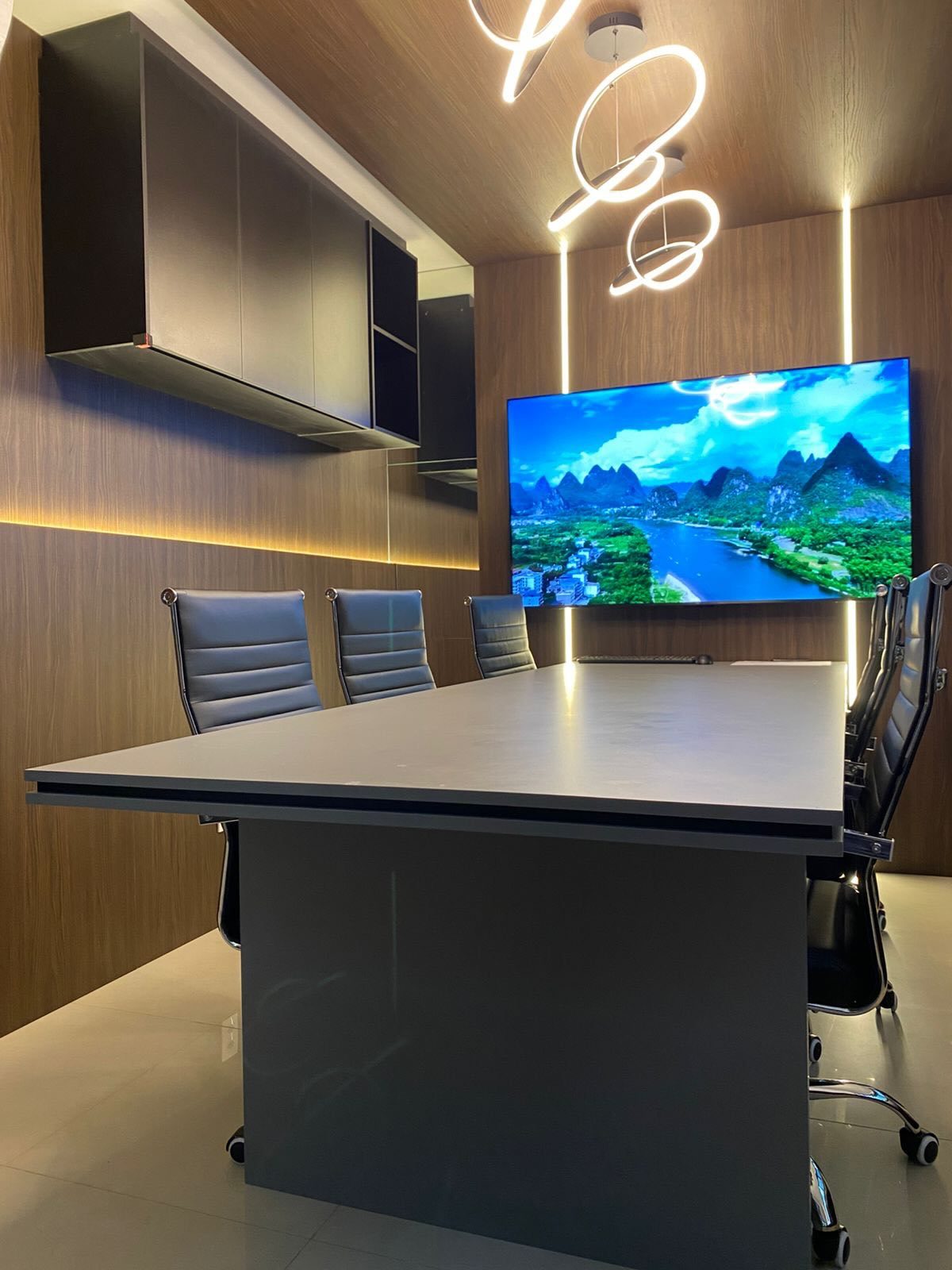 Sala de reunião com painel amadeirado, mesa grafite e frisos de LED